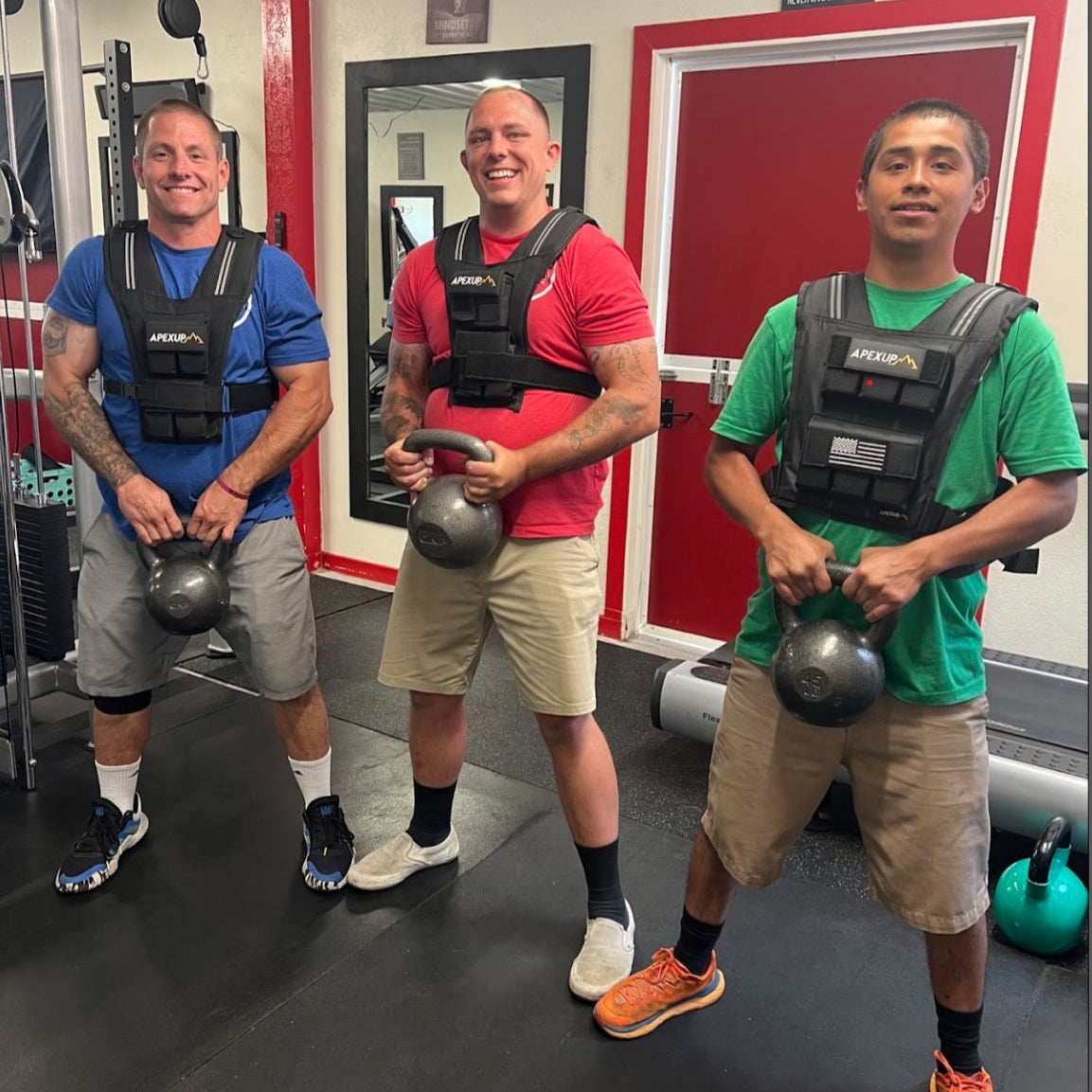 Three men in a gym setting, each holding a kettlebell and wearing weight vests.