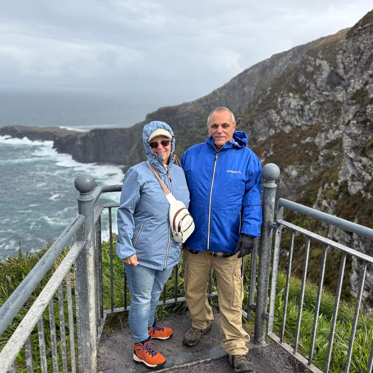 Two people who are wearing Packable Rain Jackets are standing on a cliff overlooking the ocean with a scenic view.