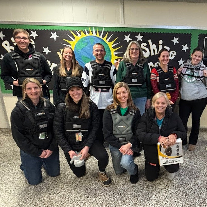 Group of people posing for a photo in a classroom setting with educational posters on the wall.